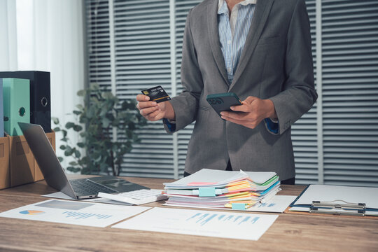 Business Transaction in Office: A businessperson is deeply focused on the intricate details of a financial transaction. They delicately hold a credit card and calculator.