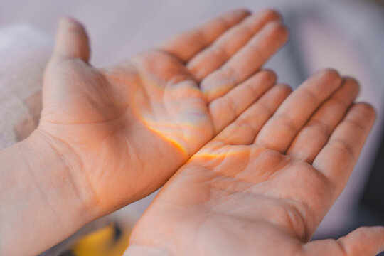 Close-up of childs open hands with soft rainbow light shining across the palms, creating a dreamy and emotional atmosphere with warm tones and shallow depth of field.