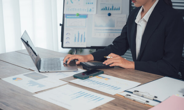 Financial Analysis: A professional delves into financial intricacies, utilizing a laptop and calculator, surrounded by charts and reports, to dissect data and formulate strategies.