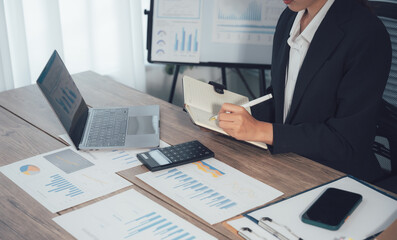 Strategic Analysis: An expert in a tailored suit meticulously reviews a series of reports, accompanied by a laptop, calculator, and smartphone on a light wood desk.