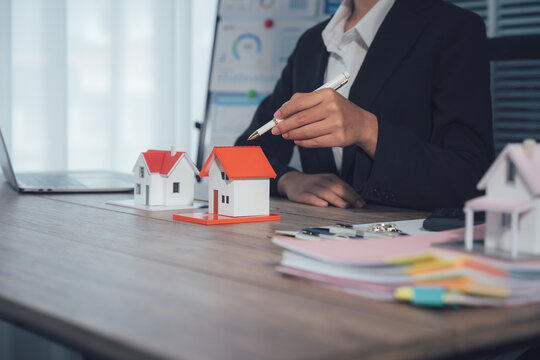 Real Estate Deal: A professional meticulously analyzes miniature model houses, symbolizing property and investment, amidst office supplies and business documents.