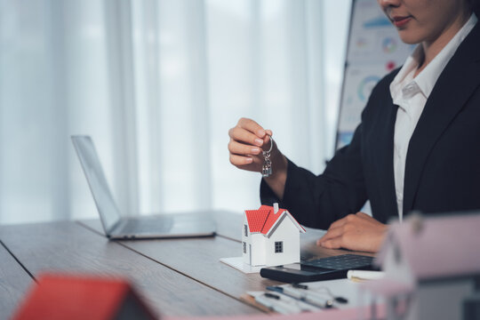 The keys to New Home: A dedicated agent's hand extends the keys to a miniature model house, symbolizing the fulfillment of homeownership dreams and the start of a new chapter. 