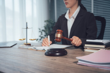 Justice in Session: A focused individual, clad in a professional suit, wields a gavel, the embodiment of legal deliberation, amidst scales of justice and law documents on a wooden desk. 