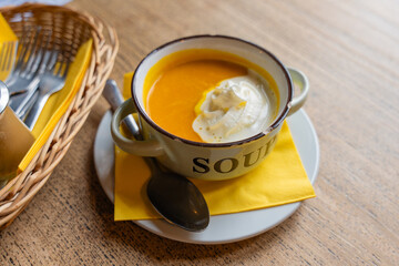 Closeup of creamy pumpkin soup with whipped cream in an enamel mug with chipped rim, placed on...