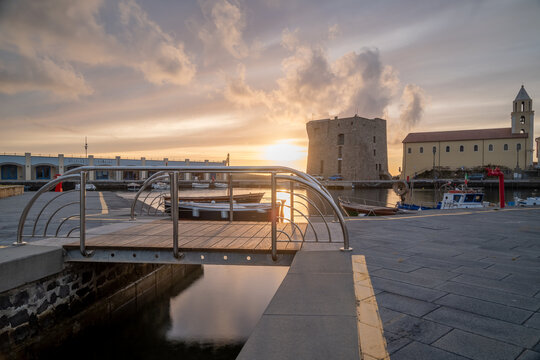 A stunning sunset at the port of Acciaroli, Italy, with a small bridge in the foreground and the historic church and tower silhouetted against the sky.