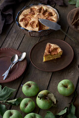 Slice of homemade apple pie served on a ceramic plate with vintage cutlery, rustic wooden table, and fresh apples from the garden