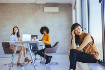 Contemplative Woman Sitting by Window During Office Meeting with Coworkers