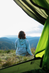 young woman back view from a tent, looking at mountain ranges and peaks, in the mountains, hiking, travel, atmospheric photo, away from everything, mental health, recovery