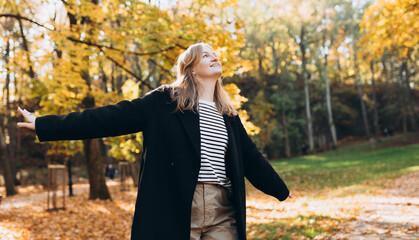 30s blonde Girl in motion expressing happiness at city park. Attractive, cheerful woman raising...