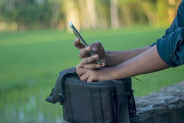 Person holding a smartphone while sitting outdoors with a camera bag