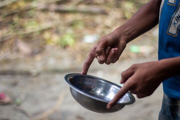 A person points to an empty metal bowl, suggesting poverty or need
