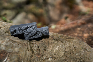 Handmade artisan black soap bars displayed outdoors with a forest background. Natural, organic, and eco-friendly skincare, vegan and plant-based, designed for sustainable self-care, holistic wellness