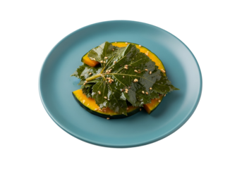 Slices of pumpkin, adorned with vibrant green leaves and sesame seeds, resting on a teal plate against a black background.