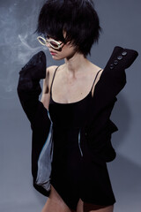 stylish woman with glasses wearing black clothing in moody lighting with smoky background and...