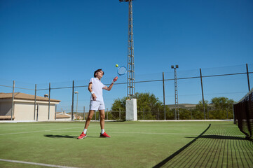 Obraz premium Young Athlete Practicing Tennis on Outdoor Court Under Clear Sunny Skies