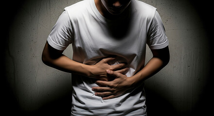 Person holding stomach in pain against concrete wall. Dramatic close-up about health and suffering. Digestive issues, abdominal pain, feeling sick.