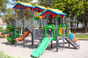 Bright plastic playset with tunnel slide, spiral slide and seesaw in a green park. Useful for education, recreation, childcare brochure, urban planning article, parenting blog or safety guide.