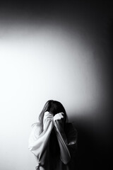 Woman hiding face in long sleeves against wall