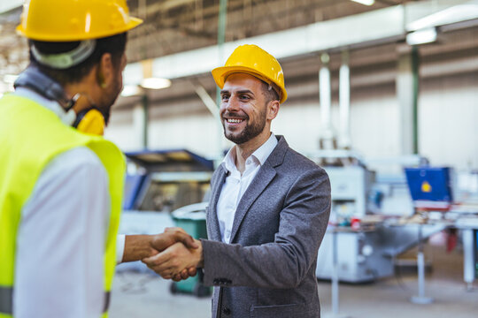 Businessmen Shaking Hands Wearing Safety Helmets in a Factory Setting