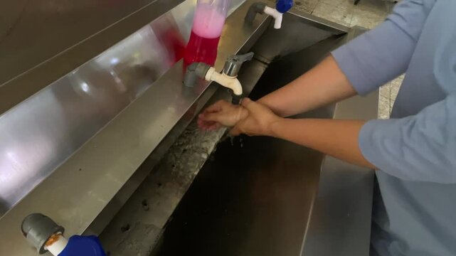 Essential Hygiene Routine: Worker Vigorously Washing Hands in a Large Industrial Stainless Steel Sink