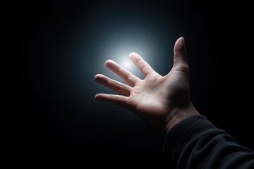 Hand reaching towards glowing light in darkness