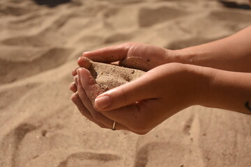Human hands holding and pouring sand, symbol of time and fleeting moments, beach background.