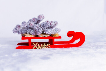 Red Christmas sleigh with snow-covered branches and “XMAS” detail on a white snowy background