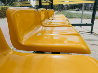 Row of yellow plastic seats at bus stop shelter on urban sidewalk, public transportation...