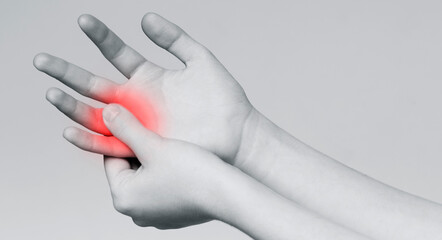 Young woman suffering from pain in hand and massaging her painful finger, monochrome panorama