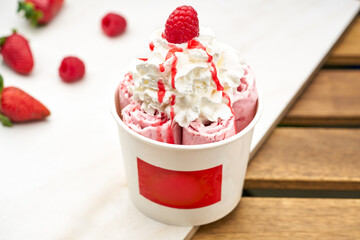 Strawberry Rolled Ice Cream with Whipped Cream and a Raspberry on top in White Cup closeup side view on table
