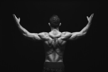 Fototapeta premium Unrecognizable man bodybuilder shows strong hands and back muscles, athletic trapezius, studio shot on black background, black and white image.