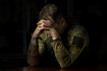 A soldier in handcuffs sits in the dark, covering his face with his hand.