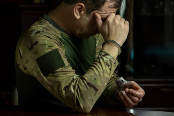 A soldier in handcuffs bows his head towards his hands.