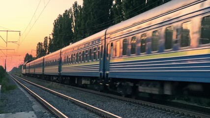 Long Distance Passenger Train Moving Through Rural Countryside During Summer Sunset | Blue White Railway Cars on Tracks with Golden Evening Light | Intercity Transportation Journey