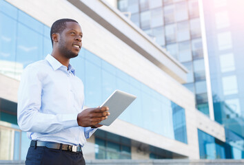 Fototapeta premium Confident successful black businessman with tablet outdoors. African-american executive taking a city walk at lunch time, urban area background