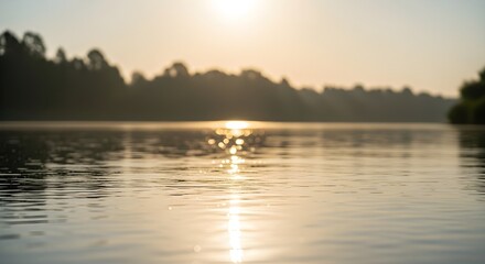 Peaceful early morning golden hour scenery reflecting over calm water on a misty morning at the lake with trees and clear skies in the background.