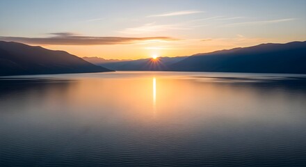 Golden sunrise over a calm lake, reflecting the sun's rays and silhouetted mountains, creating a serene landscape.