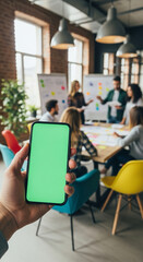 Hand showing smartphone with green screen in a trendy startup office with brainstorming team.