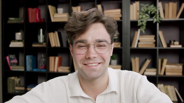 Portrait of a handsome young boy with glasses looks at the camera and smiles discreetly. Dark-haired student slightly nods his head demonstratively looking into the camera.