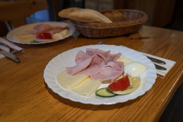 Ham, cheese, and eggs on a white plate with a bread basket in the background.
