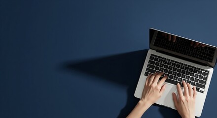 Overhead shot of hands typing on a laptop computer against a dark blue background.