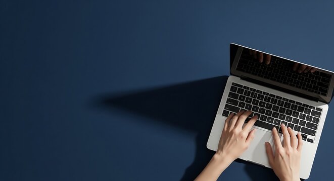 Overhead shot of hands typing on a laptop computer against a dark blue background.