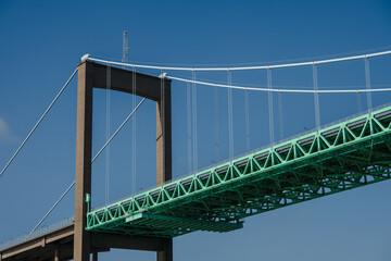 Suspension bridge tower and green trusses against clear sky.
