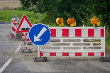 A plastic barrier and a circular metal road sign for a detour inserted into a base by the road.
