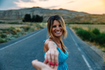 Naklejka premium Smiling woman leading partner by hand on scenic road trip