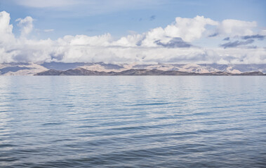 Panorama landscape of Lake Karakul in the Pamir mountains in the Tien Shan against the background of high snowy rocky peaks with clouds, morning panorama of the lake for the background