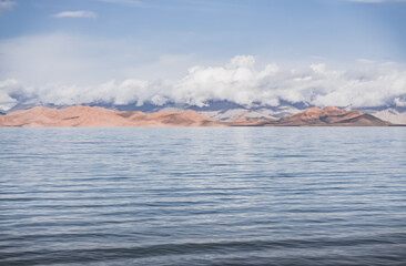 Panorama landscape of Lake Karakul in the Pamir mountains in the Tien Shan against the background of high snowy rocky peaks with clouds, morning panorama of the lake for the background