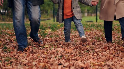 Cheerful family playing in park with autumn leaves walk nature with child. Legs, Family child mother father walking in autumn park kicking yellow dry leaves with their feet. Family on rest in nature