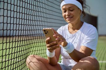 Woman Relaxing on Tennis Court Using Smartphone After Training