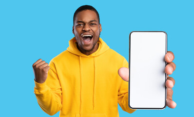 Emotional african american guy gamer showing smartphone with blank screen and celebrating success,...